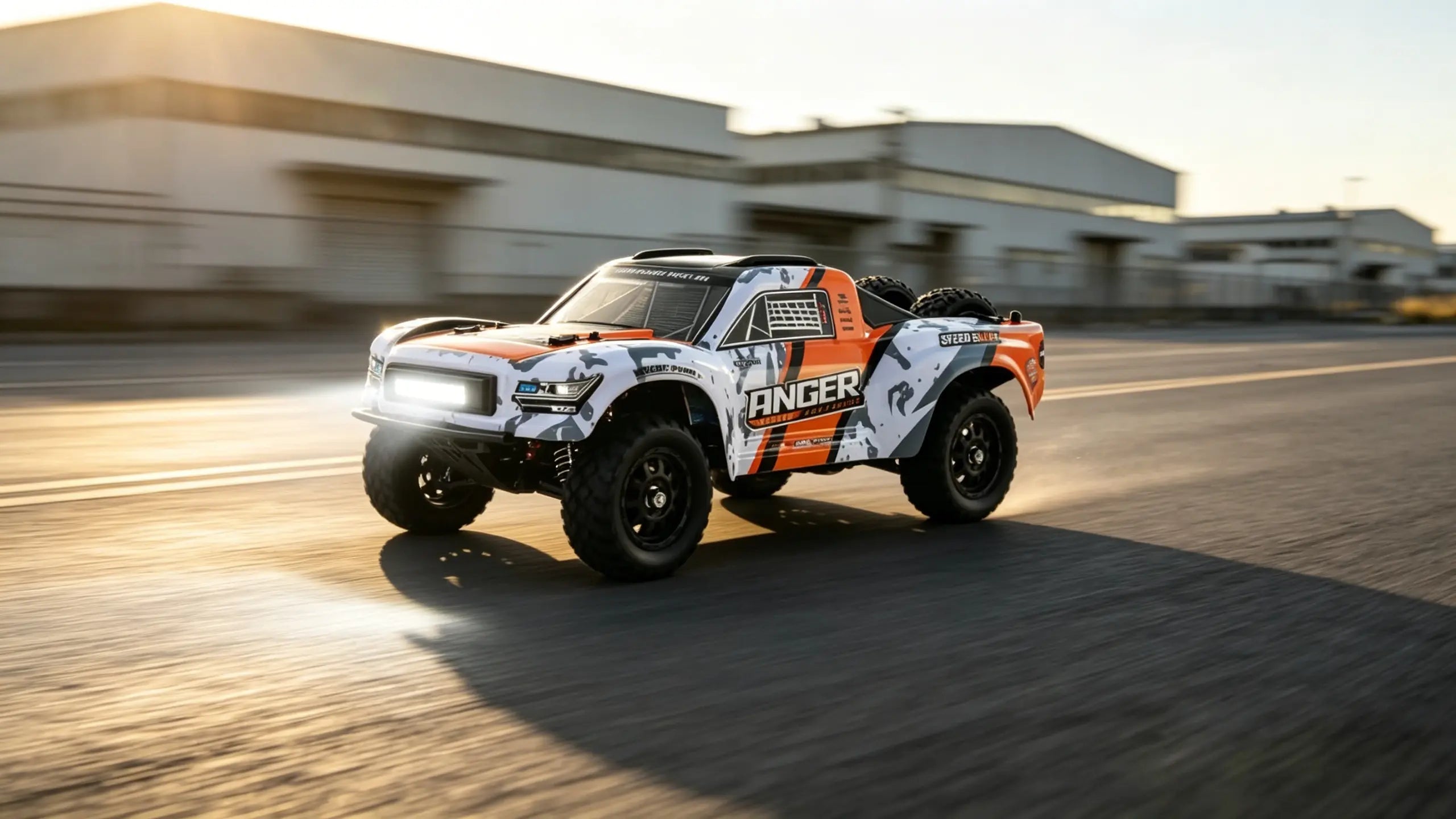 A high-speed Racing RC Truck with a striking white, orange, and black “RACER” livery, captured in motion as it speeds and kicks up dust on a road.